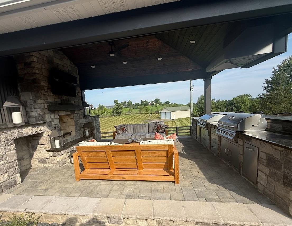 NuWave covered outdoor living area with stone fireplace, seating, and built-in grill