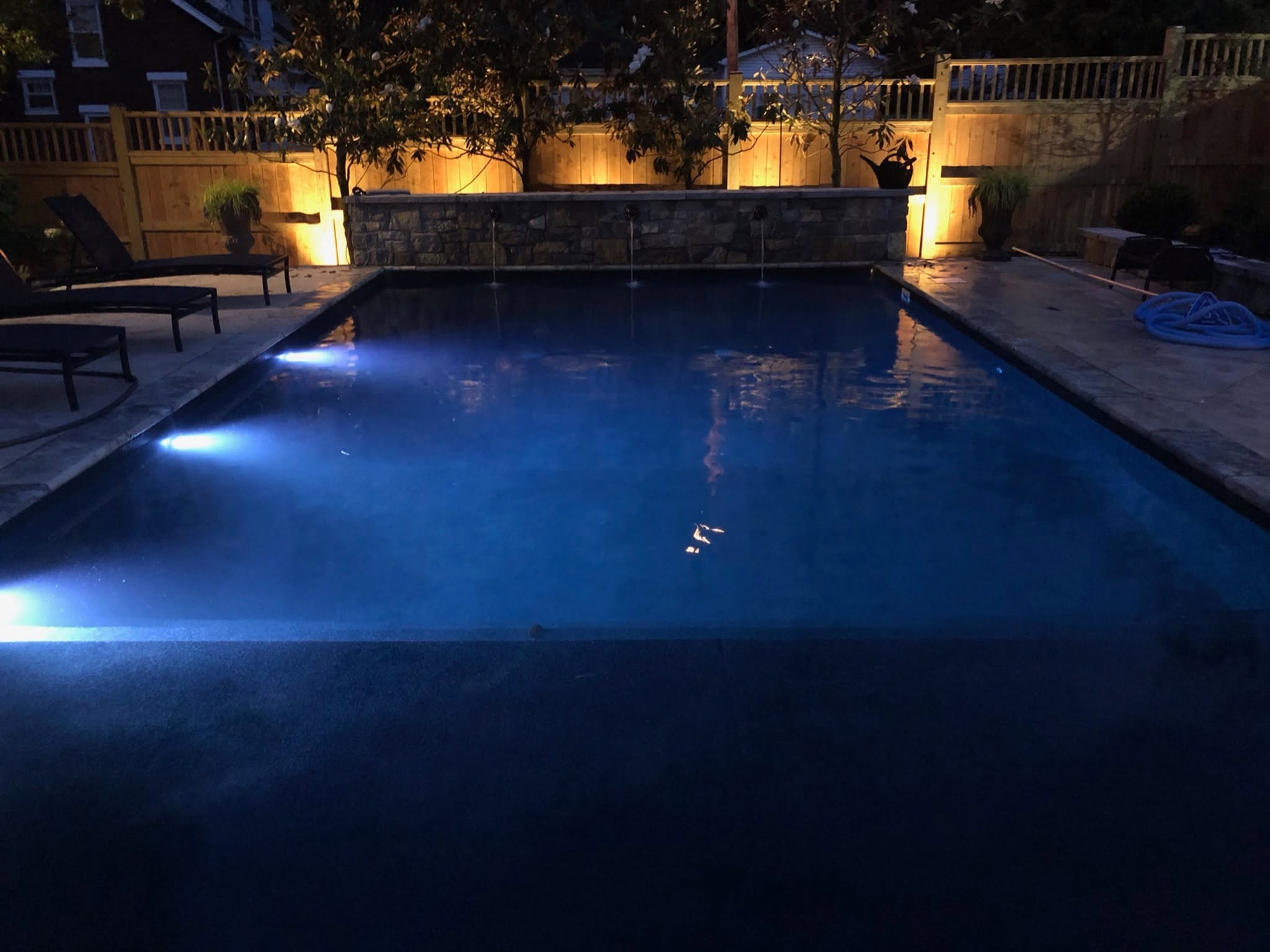 NuWave swimming pool illuminated at dusk with a stone water wall